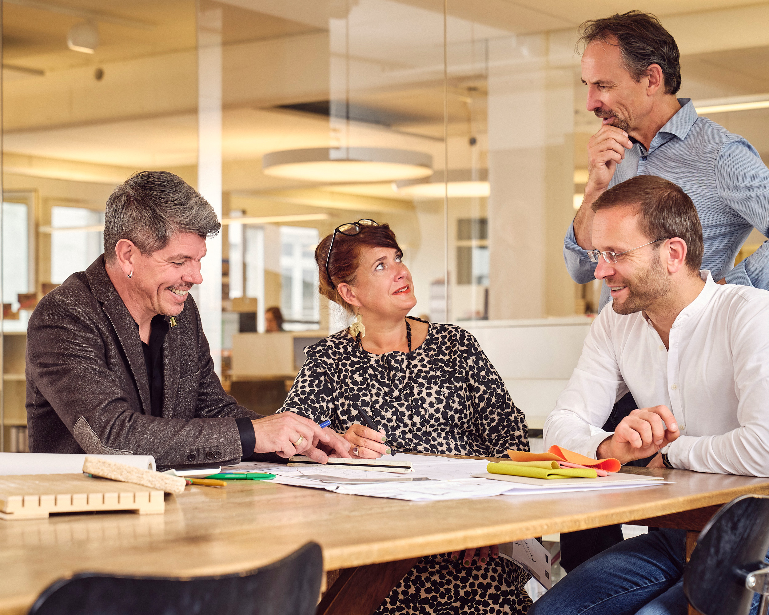 Architekten sitzen udn stehen an einem Besprechungstisch und diskutieren über eine Zeichnung