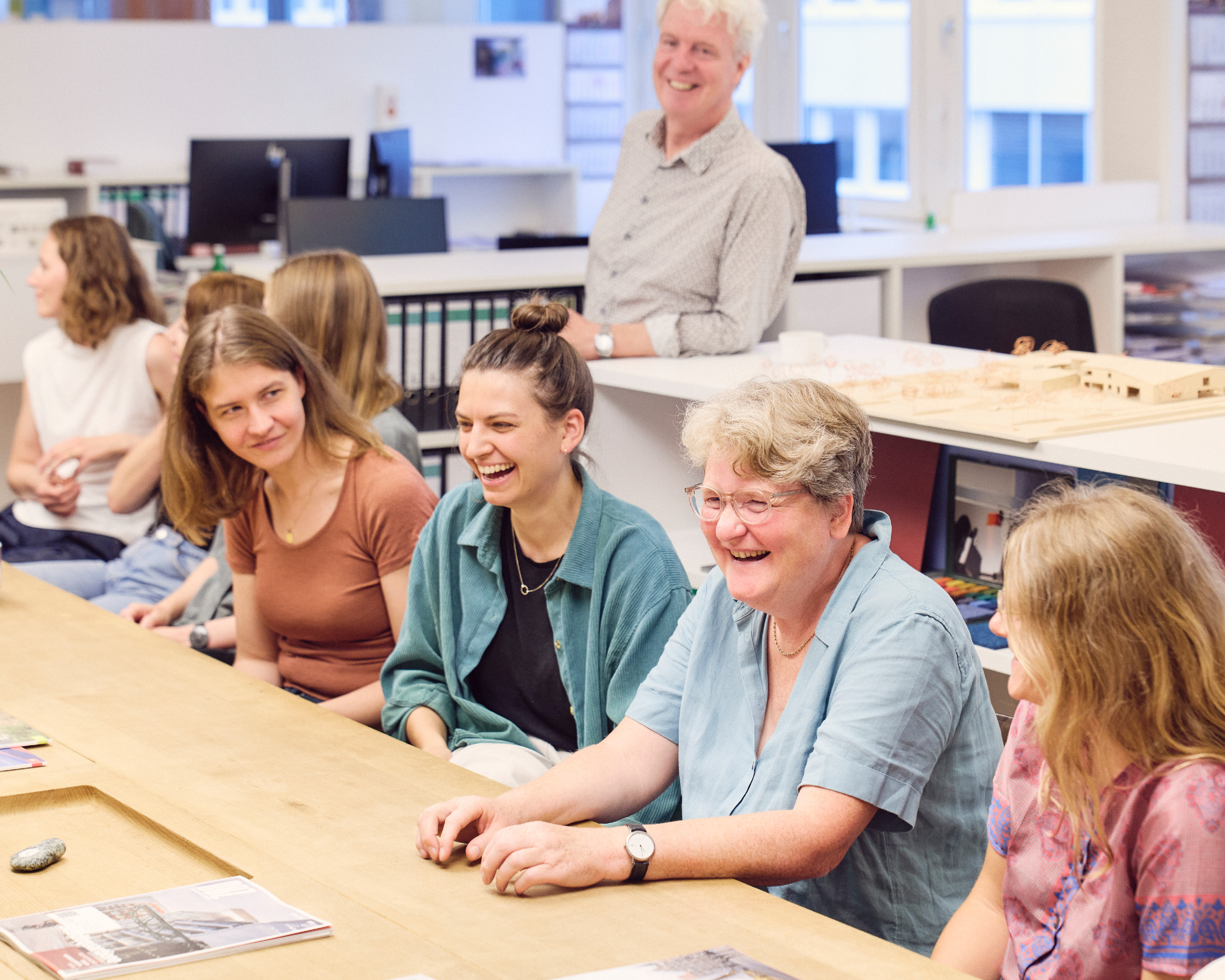 Fröhliche Menschen an einem Besprechungstisch bei Trapez Architektur