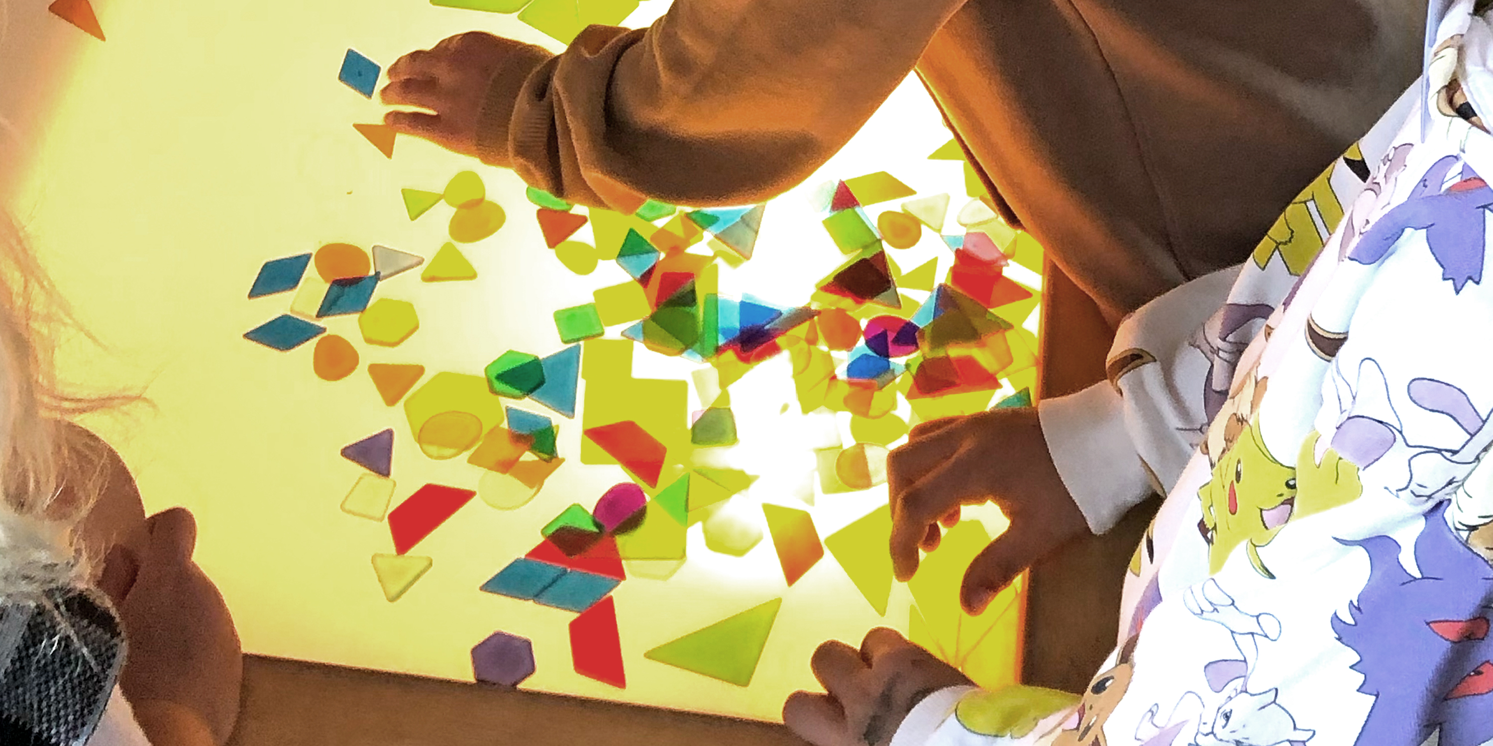 Hände von Schulkindern, die geometrische Formen auf einem Leuchttisch anordnen