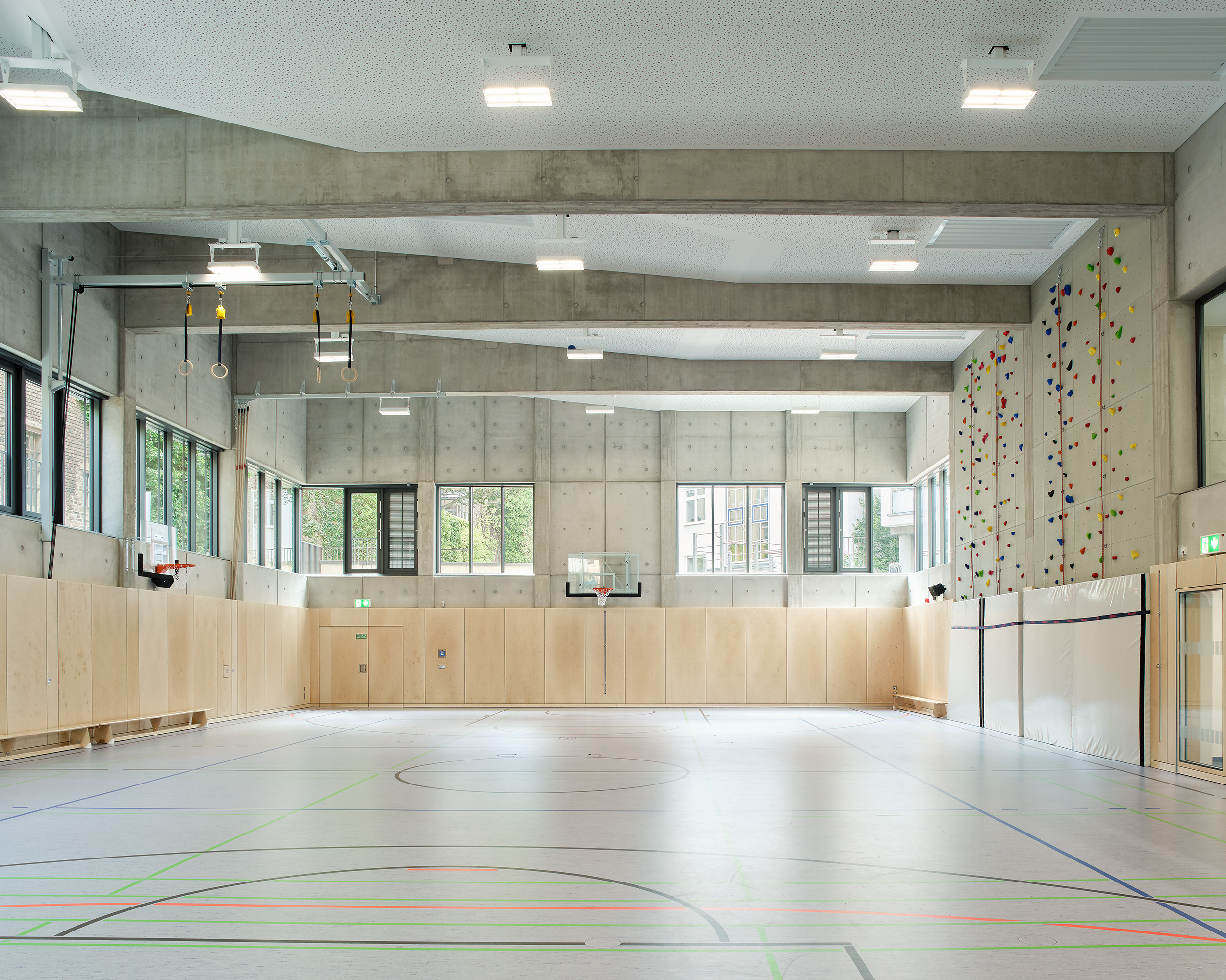 Innenaufnahme einer Sporthalle mit Holzprallwänden, Kletterwand und sichtbarer Dachkonstruktion aus Stahlbeton.