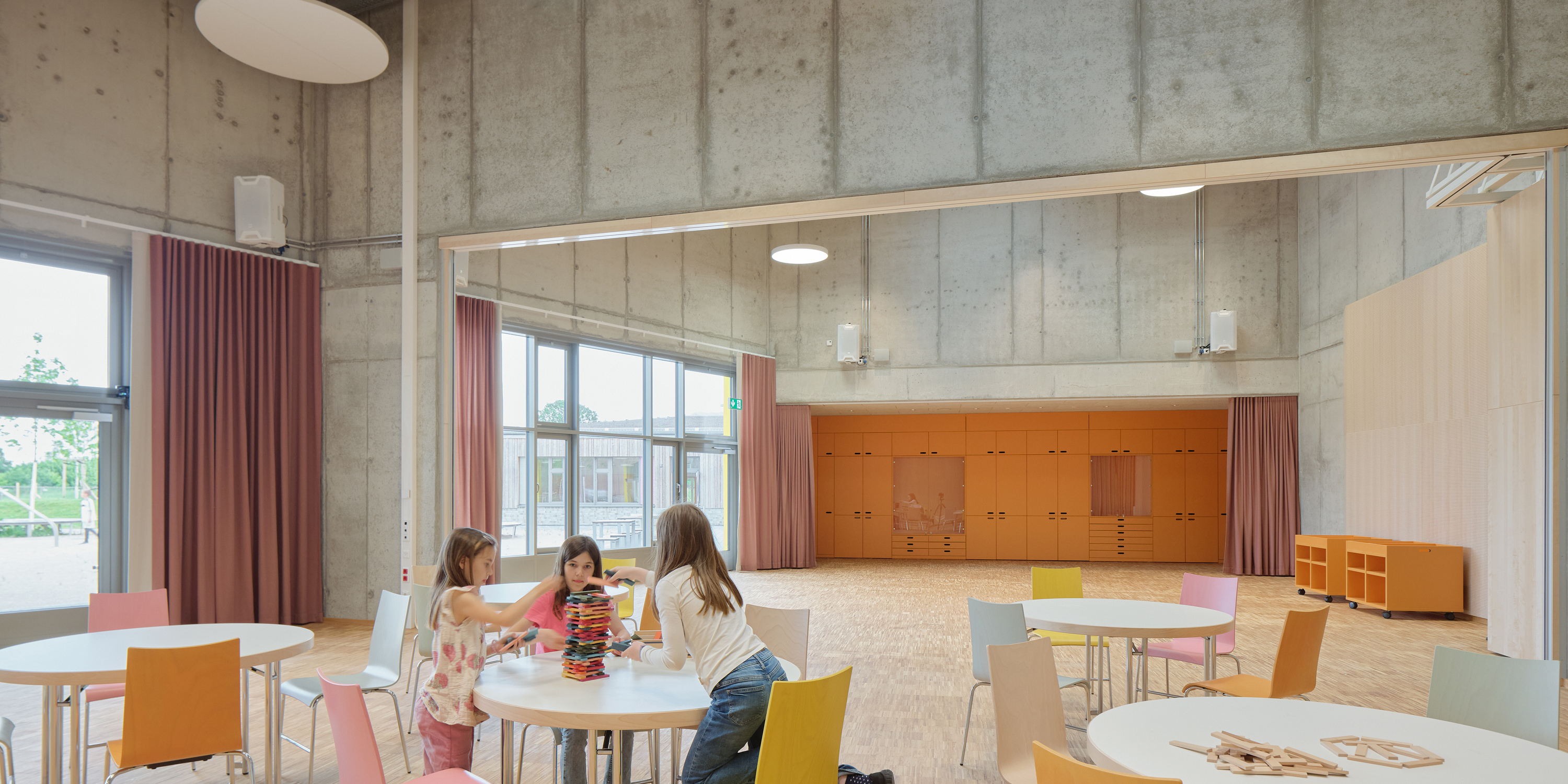 Kinder sitzen an einem runden Tisch in einer Mensa einer Schule und spielen