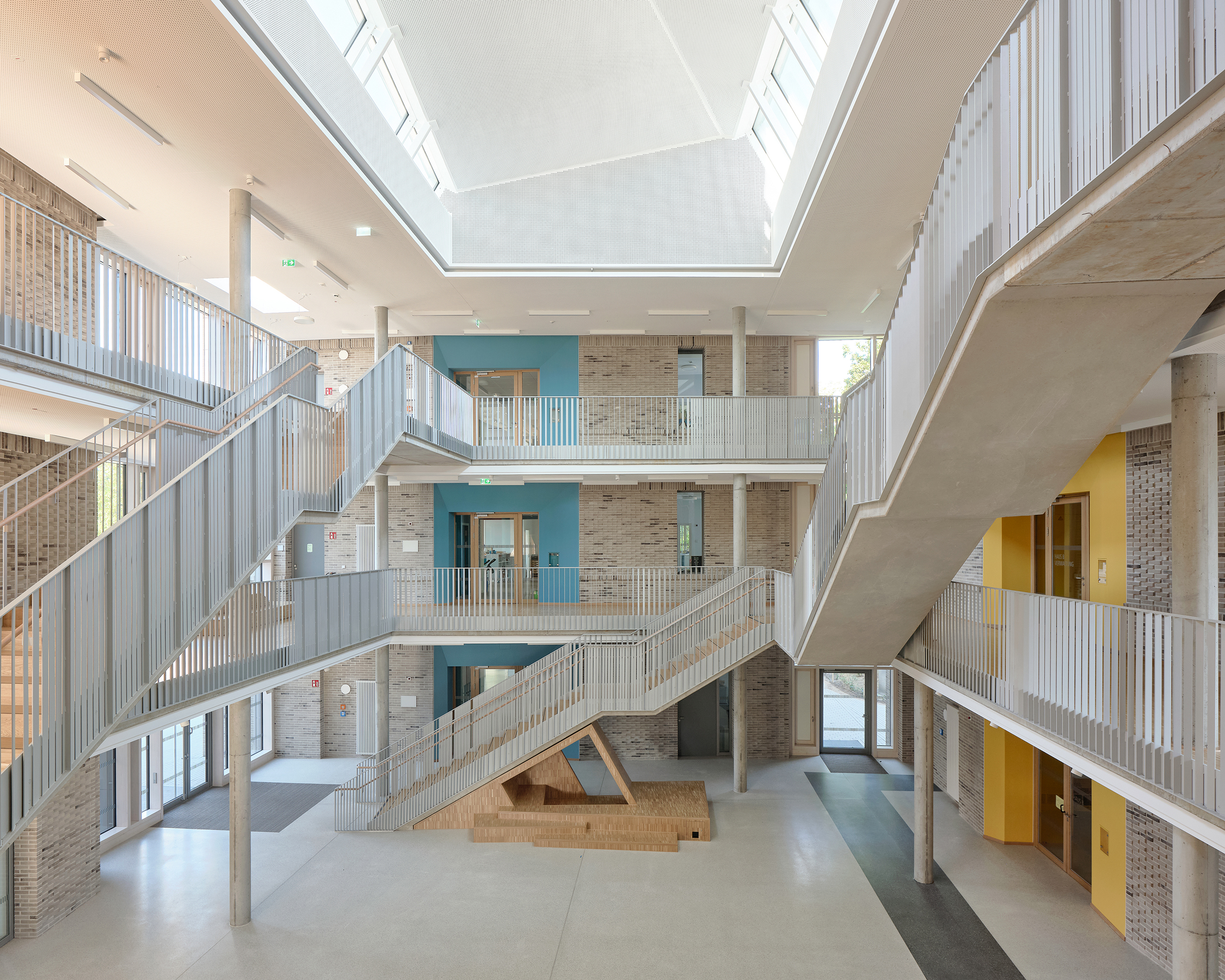 Ein Atrium in einer Schule mit großem Oberlicht, Treppen in unterschiedlichen Richtungen, Galerien und einem Einbaumöbel.